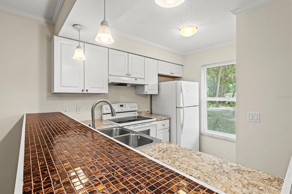 A kitchen features white cabinets, a granite countertop, a tiled breakfast bar, and white appliances — 4631 SUMMERWIND DRIVE UNIT 16, SARASOTA, FL