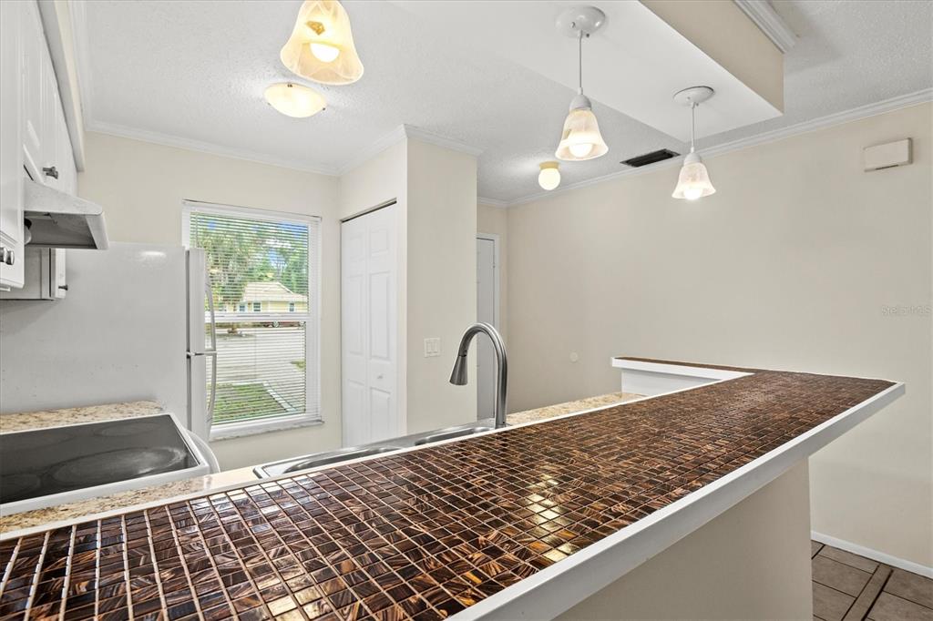 A kitchen features a tiled breakfast bar, stainless steel faucet, and pendant lighting — 4631 SUMMERWIND DRIVE UNIT 16, SARASOTA, FL