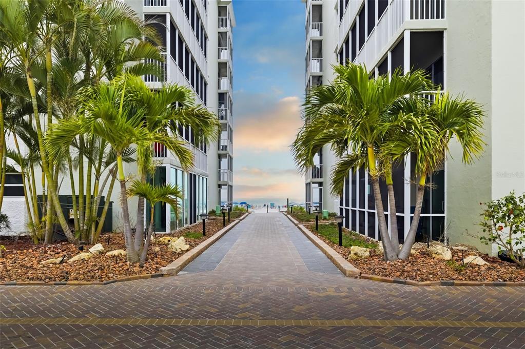 A paved walkway leads between two tall apartment buildings toward a sandy beach — 6312 MIDNIGHT PASS ROAD UNIT 305S, SARASOTA, FL