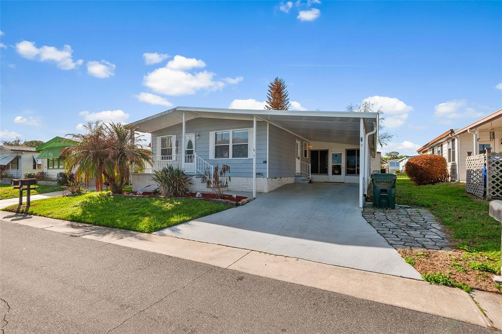 A light blue single-story mobile home features a carport, front porch, and a grassy lawn — 914 PINE RIDGE DRIVE, LAKELAND, FL