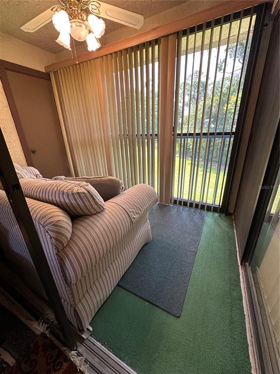 A sunroom features a striped armchair, a ceiling fan, and vertical blinds over sliding doors — 3279 WESTRIDGE BOULEVARD UNIT 204, ORLANDO, FL
