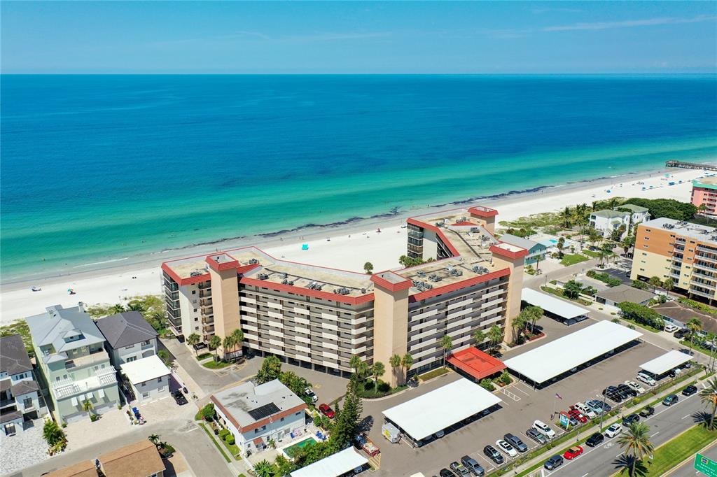 An aerial view shows a multi-story beachfront condominium complex with a parking lot — 18304 GULF BOULEVARD UNIT 116, REDINGTON SHORES, FL