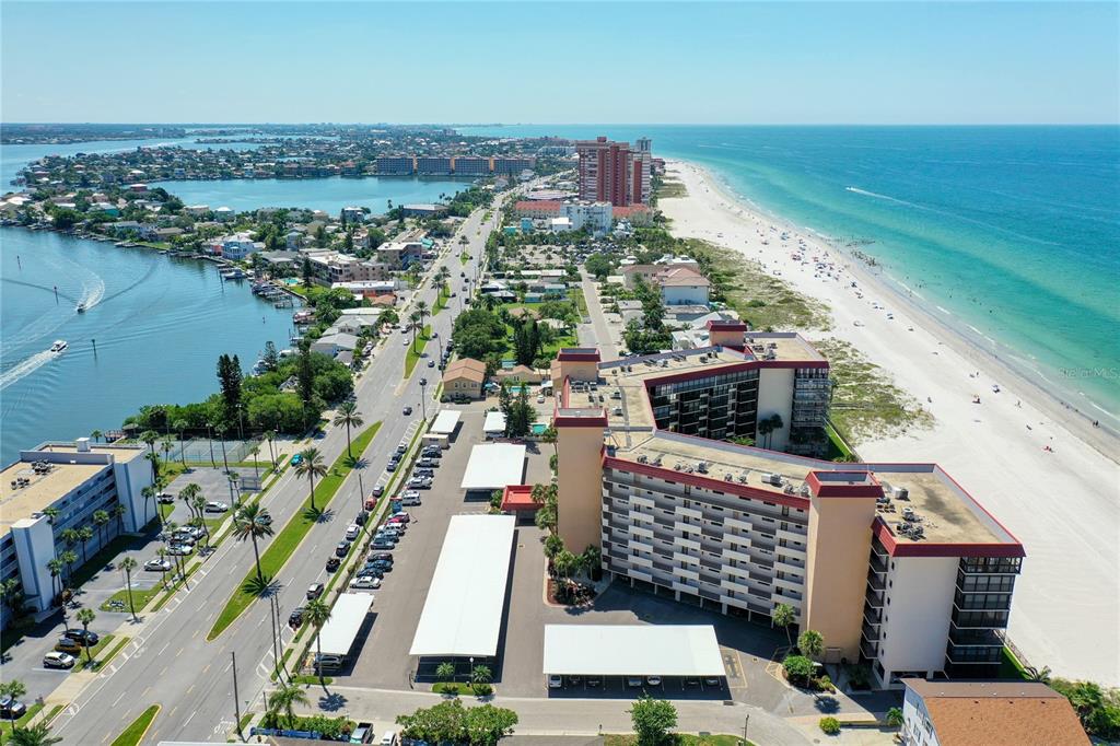 An aerial view shows a beachfront condominium complex, parking lots, and a coastal road — 18304 GULF BOULEVARD UNIT 116, REDINGTON SHORES, FL