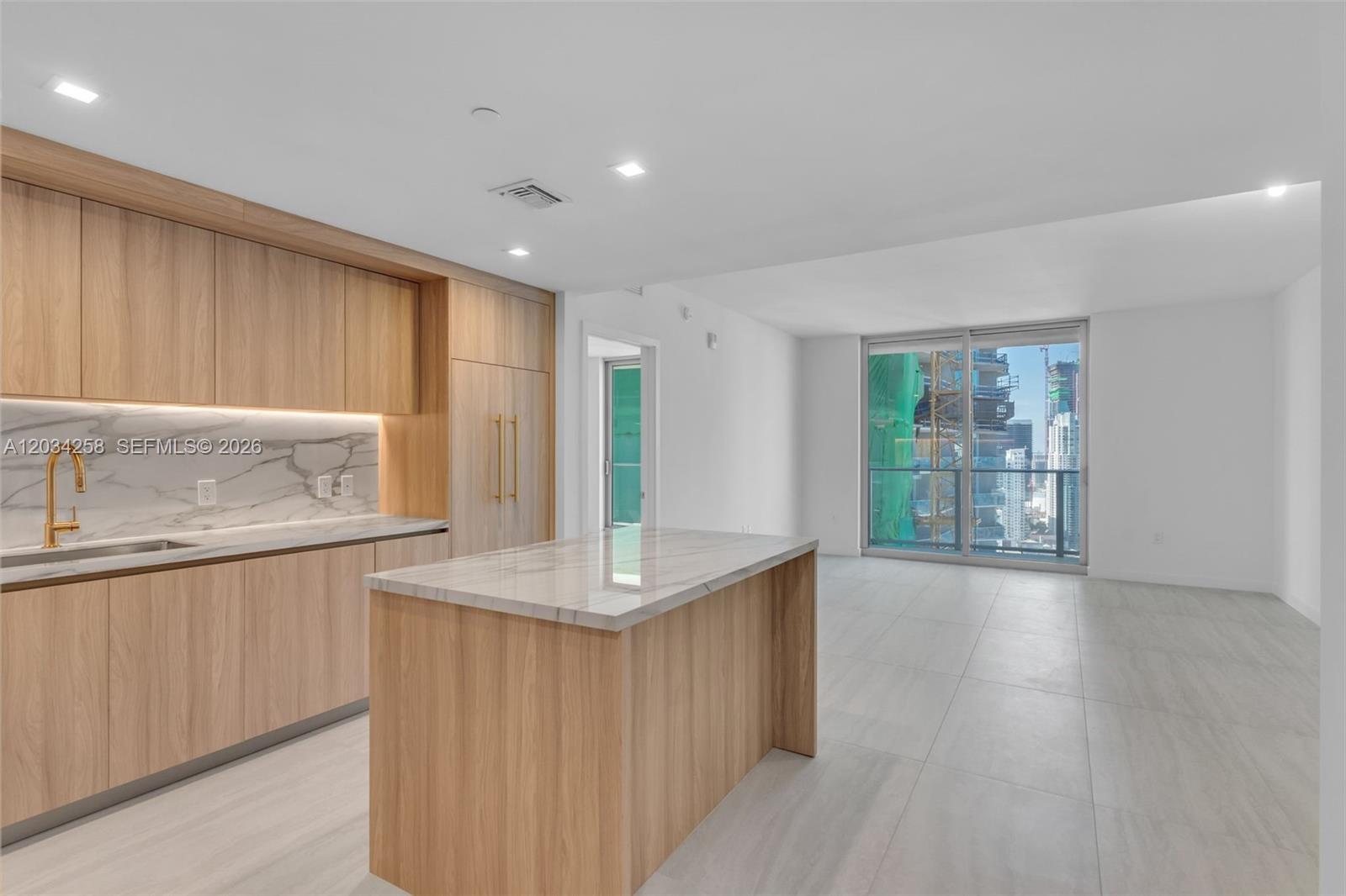 A modern kitchen with light wood cabinetry, marble countertops, and a central island faces a living area — 77 SE 5 th st, Miami FL 33131, MIAMI, FL