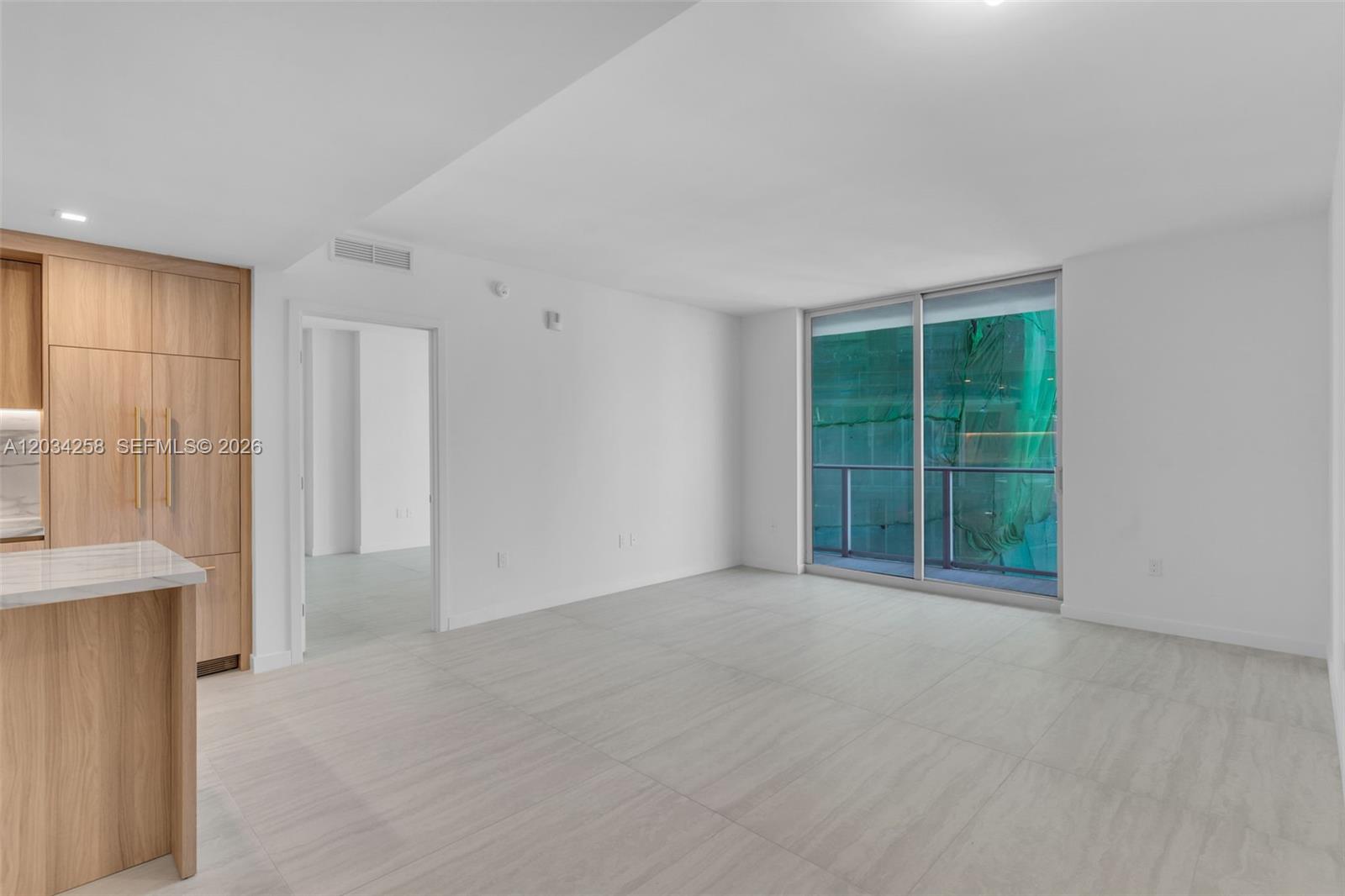 This living area features light wood cabinetry, large floor tiles, and a sliding glass door — 77 SE 5 th st, Miami FL 33131, MIAMI, FL