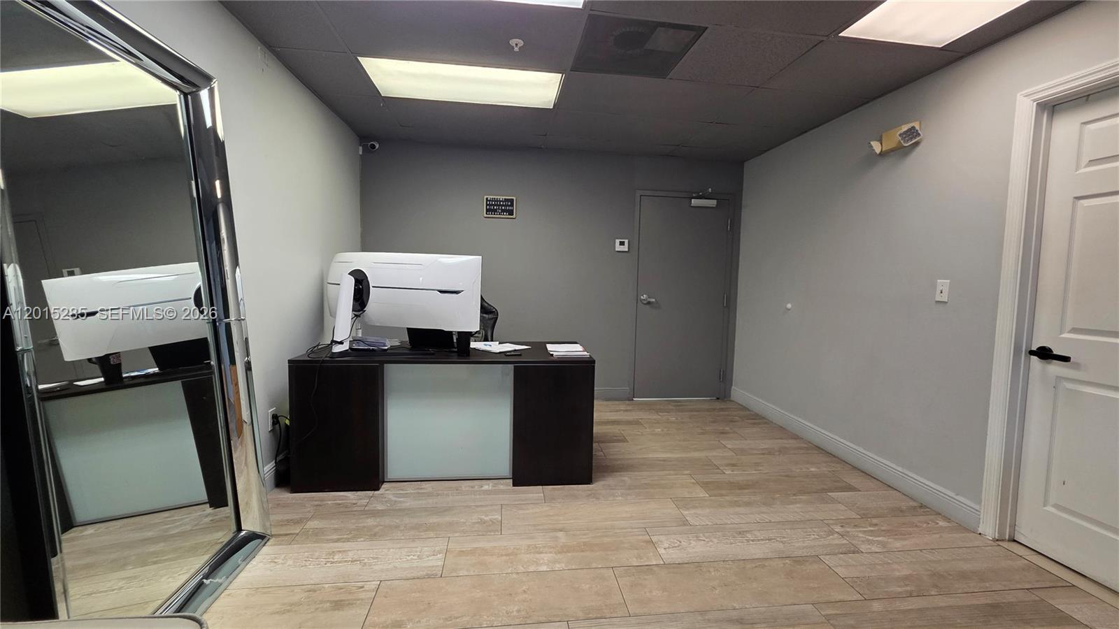 A small office features a dark desk, a computer monitor, and light wood-look tile flooring — 7762 NW 46th St, Doral FL 33166, DORAL, FL