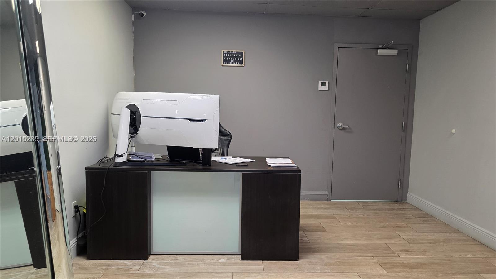 An office space features a dark wood desk, a white computer monitor, and a gray door — 7762 NW 46th St, Doral FL 33166, DORAL, FL