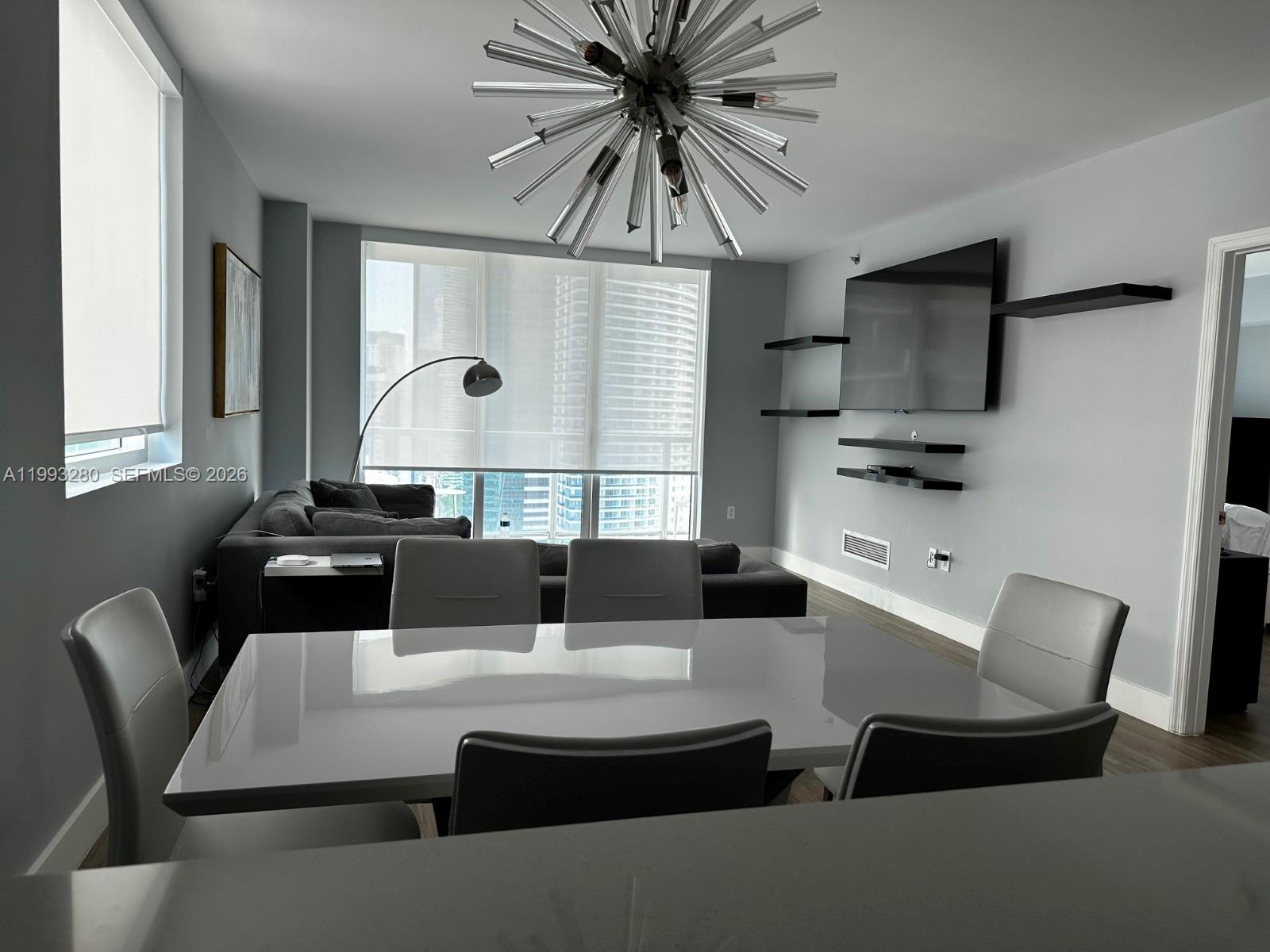 A dining area with a white table and chairs sits before a living room with a television — 500 Brickell Ave # 3307, Miami FL 33131, MIAMI, FL