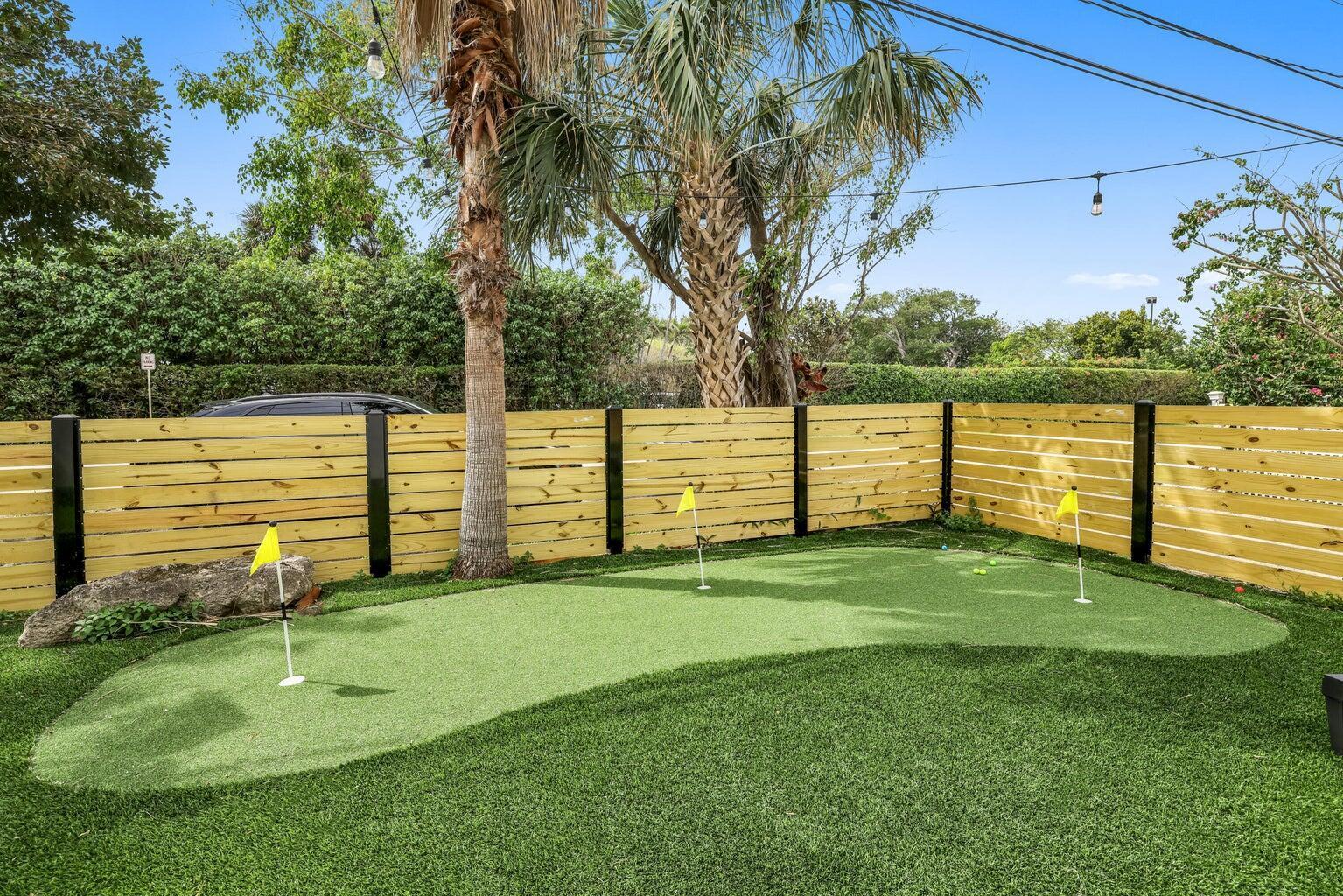 A backyard putting green with three holes and yellow flags sits before a wooden fence — 4603 N Ocean Boulevard, Boynton Beach FL 33435, BOYNTON BEACH, FL