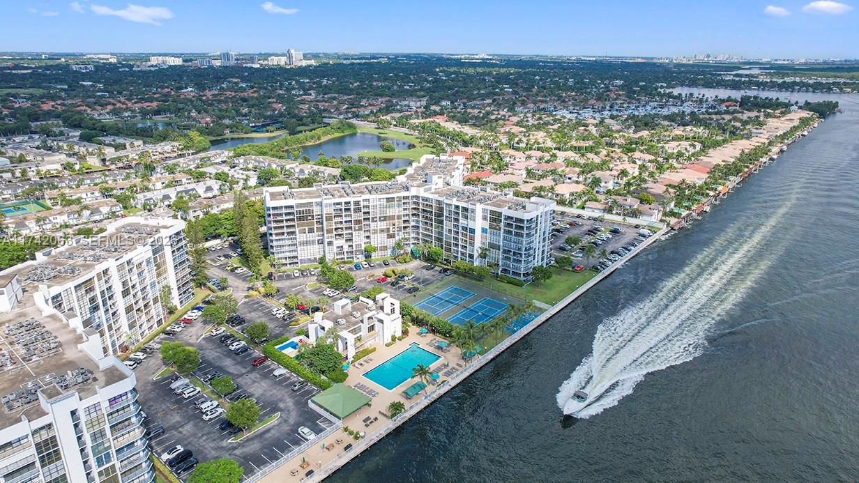 An aerial view shows waterfront apartment buildings with a pool, tennis courts, and a boat — 800 Parkview Dr # 909, Hallandale Beach FL 33009, HALLANDALE BEACH, FL