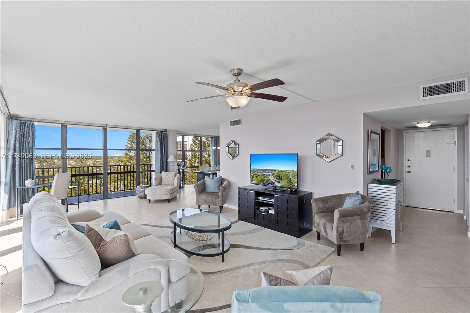 A bright living room features a glass coffee table, neutral furniture, and floor-to-ceiling windows — 800 Parkview Dr # 909, Hallandale Beach FL 33009, HALLANDALE BEACH, FL