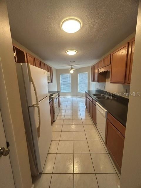 A galley-style kitchen features light wood cabinets, white appliances, dark countertops, and tiled flooring — 563 HOLBROOK CIRCLE, LAKE MARY, FL