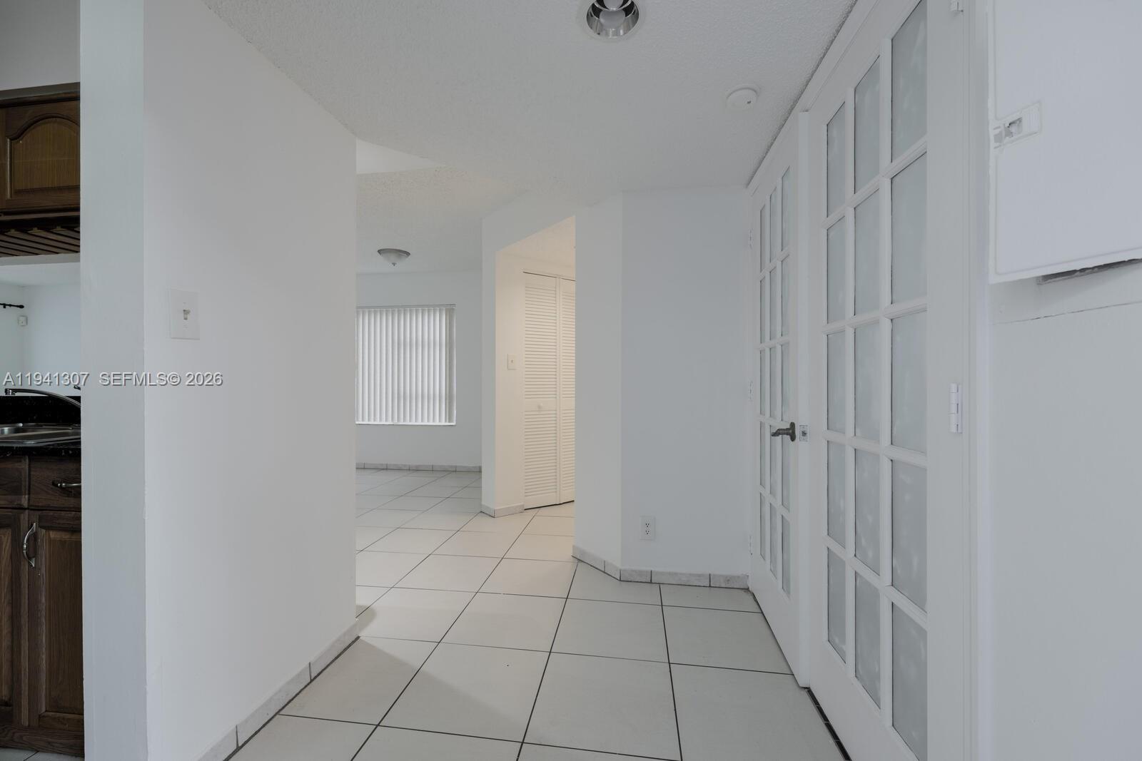 A white-tiled hallway leads toward a living area with a window and louvered closet doors — 9500 SW 140th Ct # 9500, Miami FL 33186, MIAMI, FL