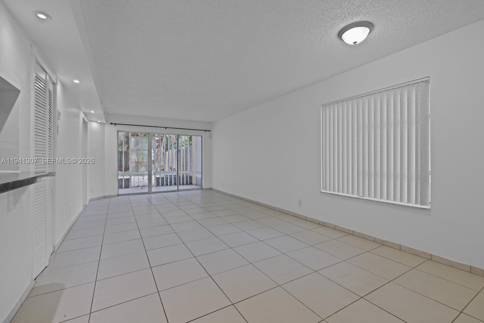 An empty room features white walls, light-colored floor tiles, a sliding glass door, and blinds — 9500 SW 140th Ct # 9500, Miami FL 33186, MIAMI, FL