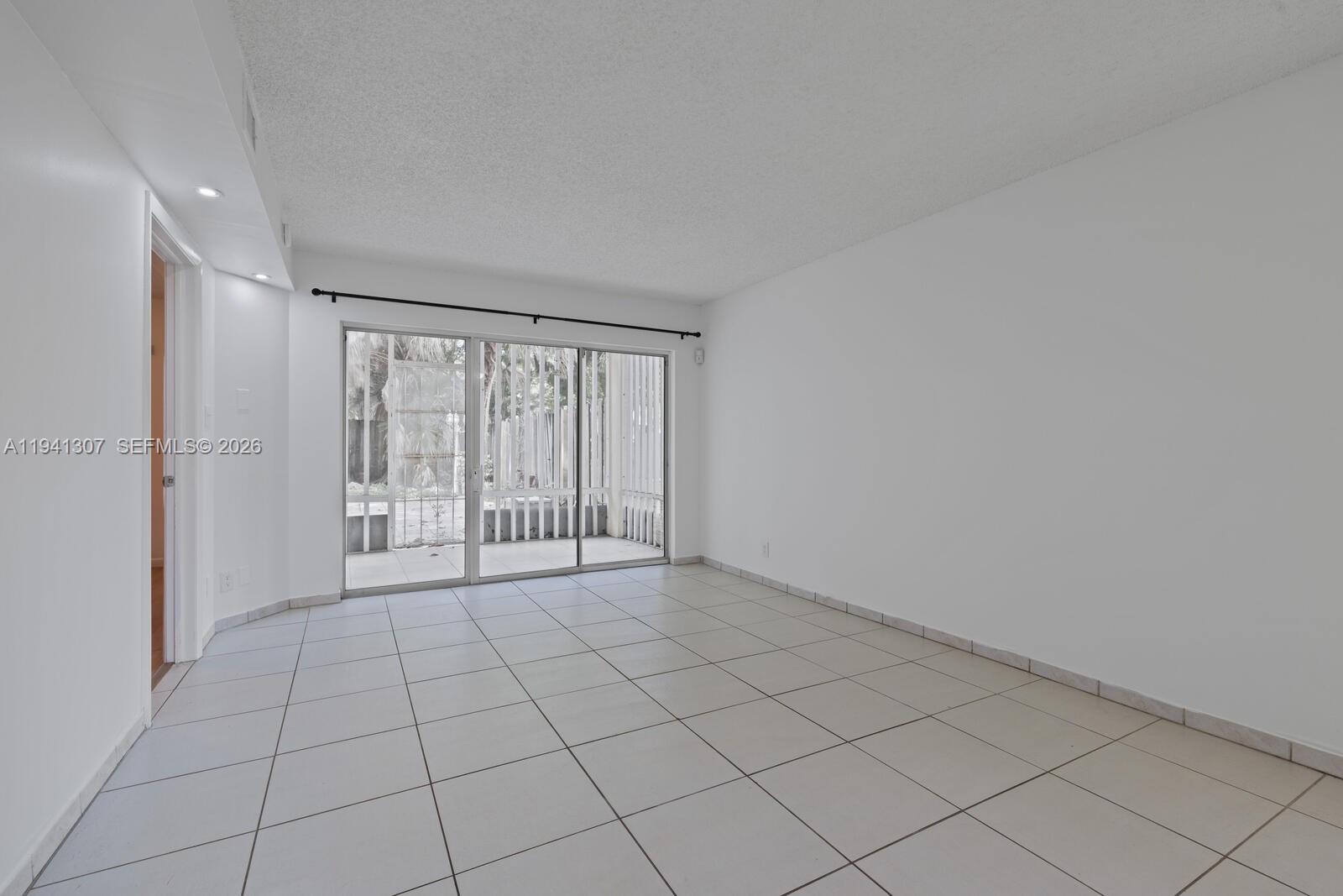A bright, empty room features white walls, light-colored floor tiles, and a sliding glass door — 9500 SW 140th Ct # 9500, Miami FL 33186, MIAMI, FL