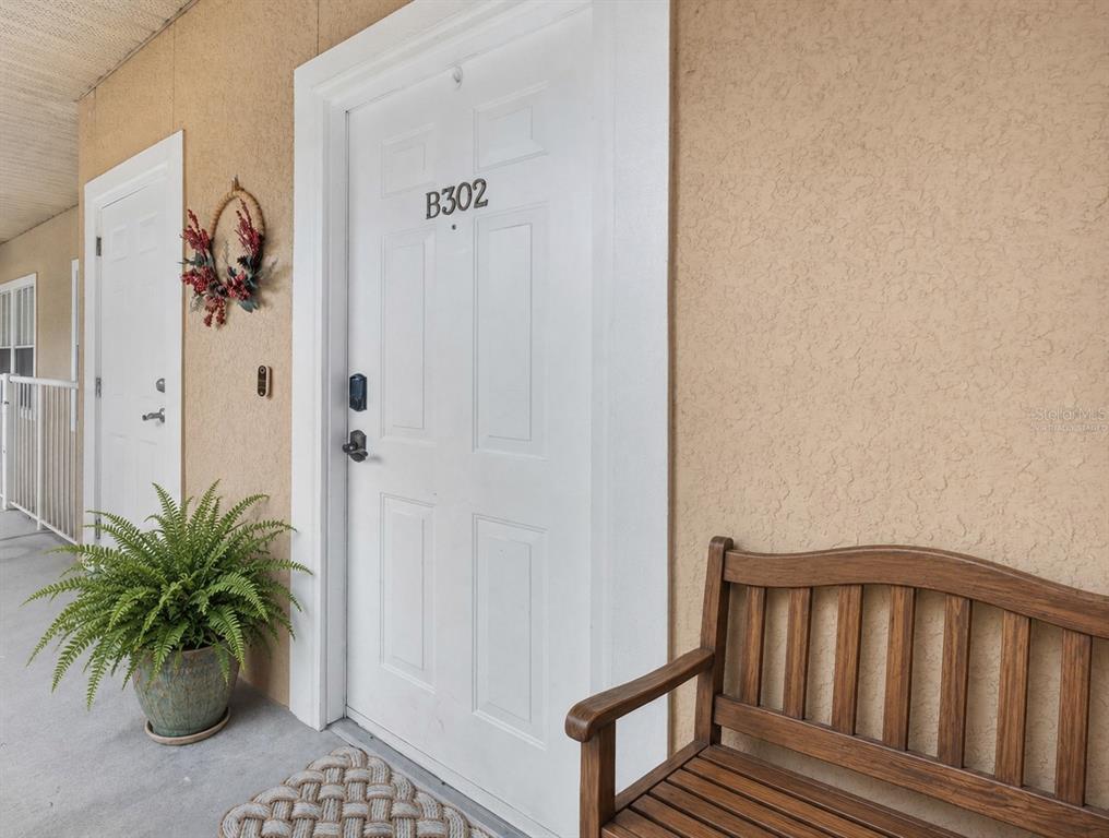 A white door labeled B302 sits on a balcony next to a wooden bench — 9124 SW 51ST ROAD UNIT 302, GAINESVILLE, FL