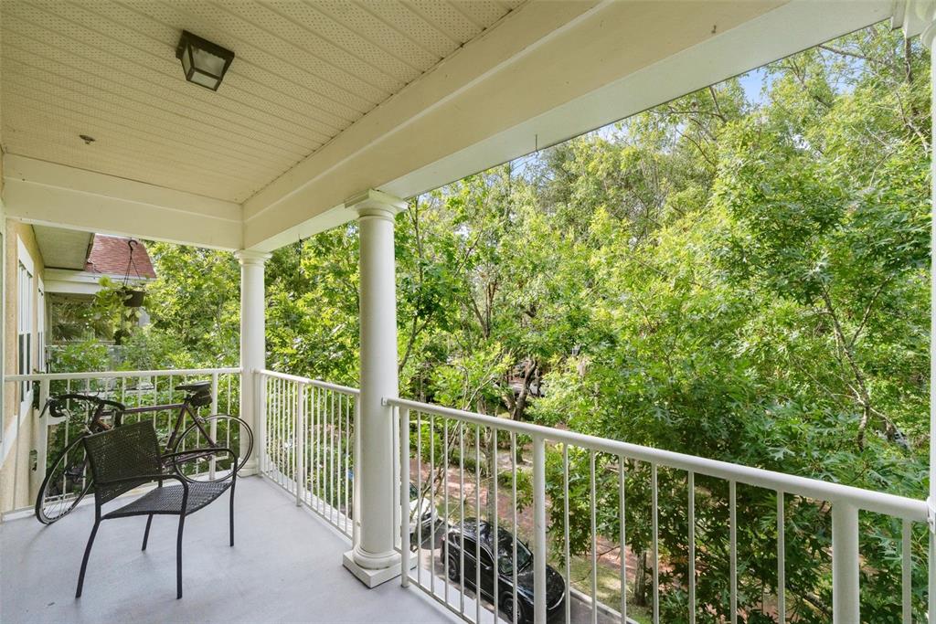 A covered balcony features a metal chair, a bicycle, white railings, and views of trees — 9124 SW 51ST ROAD UNIT 302, GAINESVILLE, FL
