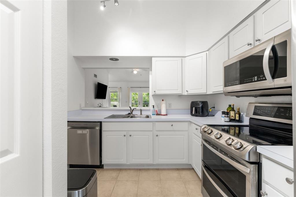 A kitchen with white cabinets, stainless steel appliances, and a pass-through window to the living area — 9124 SW 51ST ROAD UNIT 302, GAINESVILLE, FL
