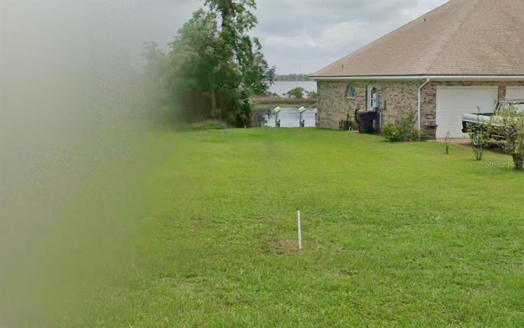 A grassy backyard extends toward a lake behind a brick house with a garage — 1990 COUNTRY CLUB DRIVE, LYNN HAVEN, FL
