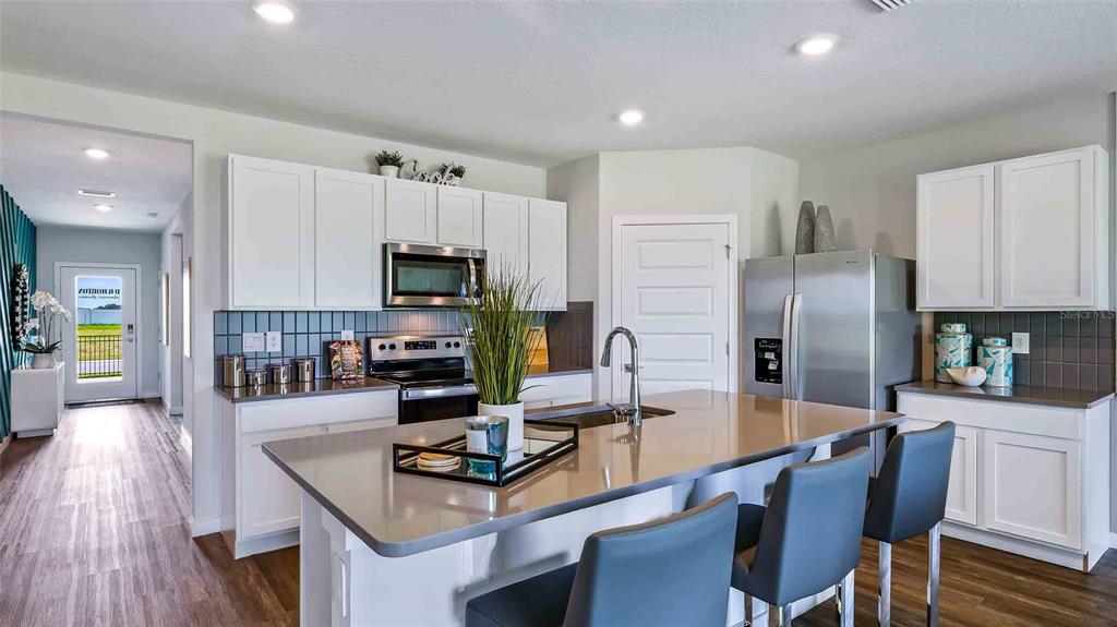 A modern kitchen features white cabinets, stainless steel appliances, a large island, and gray countertops — 18232 BEEHIVE TERRACE, LAKEWOOD RANCH, FL