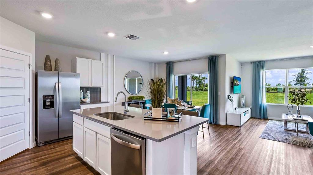 A modern kitchen with a center island and stainless steel appliances overlooks a dining area — 18232 BEEHIVE TERRACE, LAKEWOOD RANCH, FL