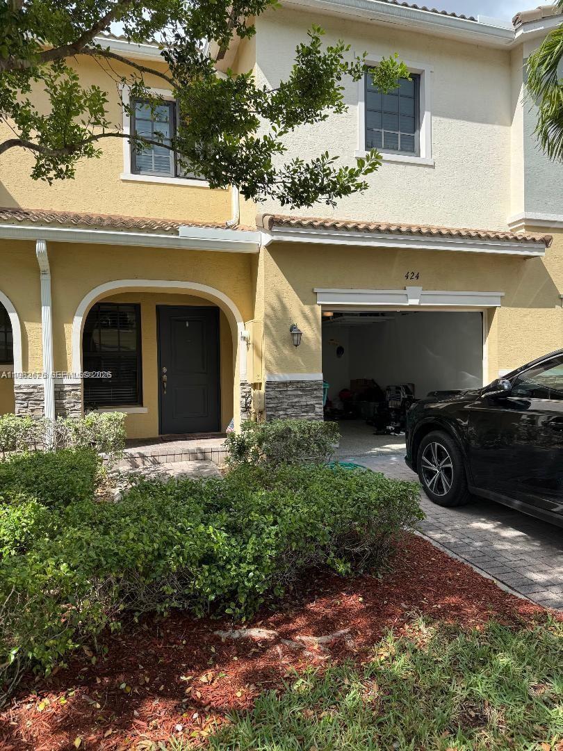 A two-story townhouse with a yellow stucco facade, a dark front door, and a garage — 424 NE 194th Ter, Miami FL 33179, MIAMI, FL