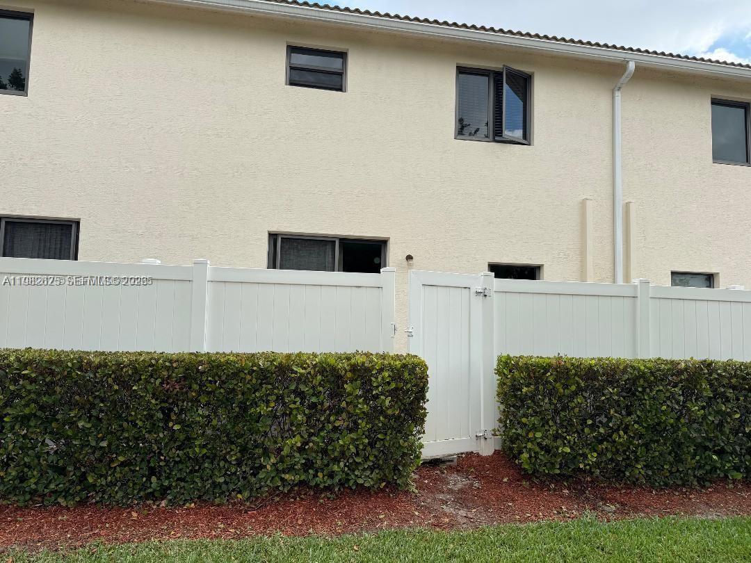 The exterior of a two-story beige stucco building features a white fence and green hedges — 424 NE 194th Ter, Miami FL 33179, MIAMI, FL