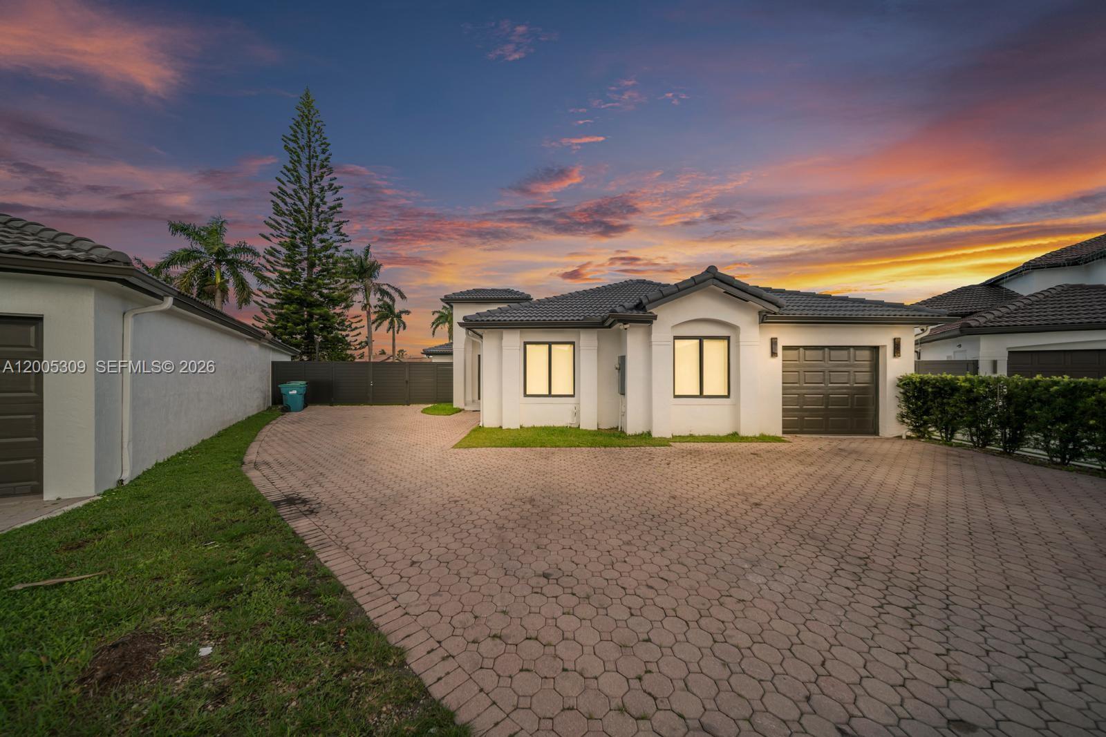 A white single-story house with a dark tiled roof and a paved driveway at sunset — 990 NW 131st Ave, Miami FL 33182, MIAMI, FL
