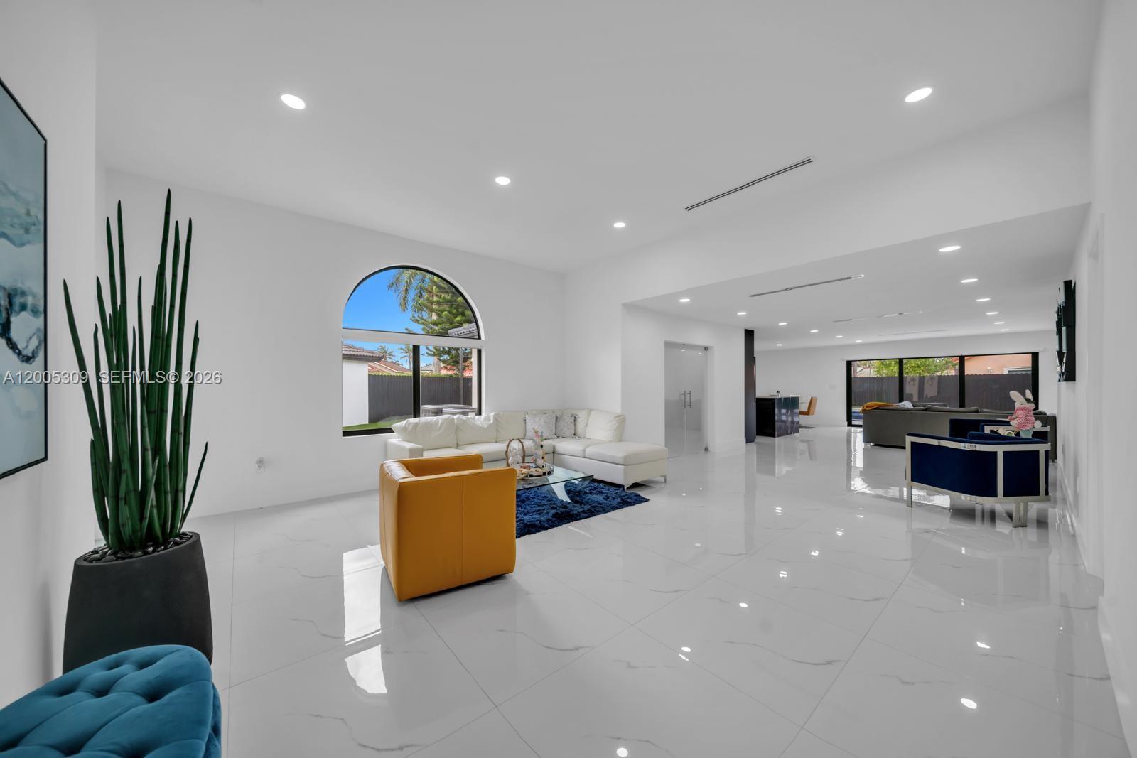 A bright, open-concept living room features white marble floors, a white sectional, and an arched window — 990 NW 131st Ave, Miami FL 33182, MIAMI, FL