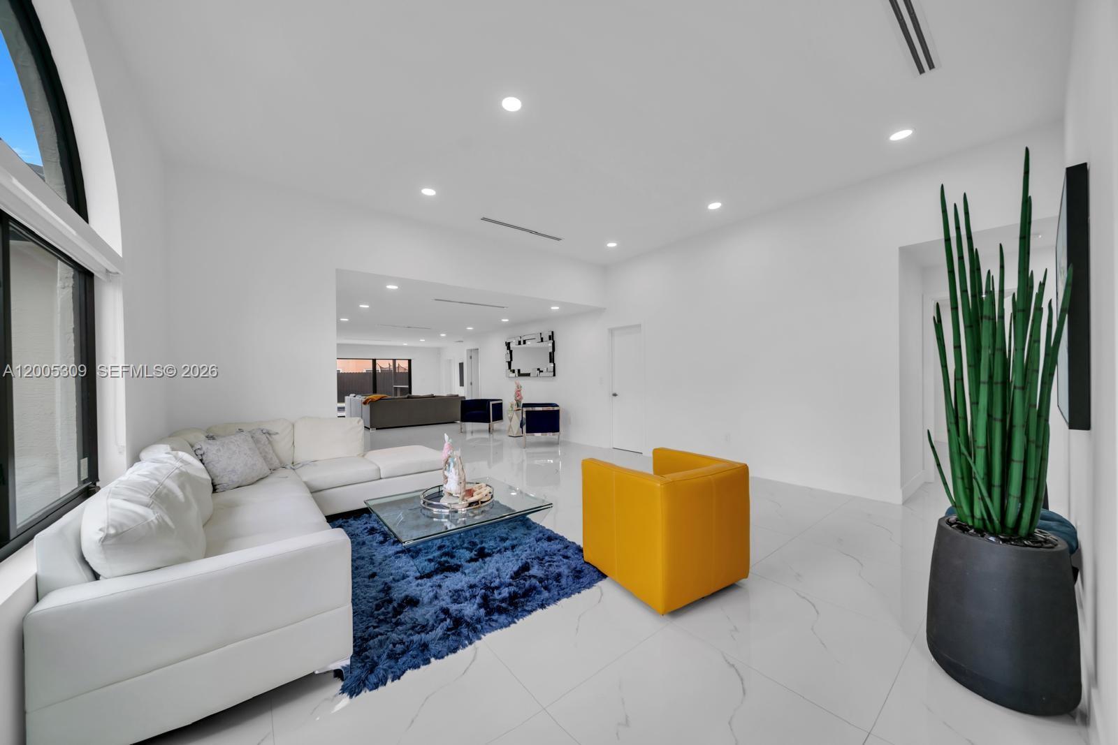 A modern living room features white walls, marble-style tile floors, a white sectional, and yellow armchair — 990 NW 131st Ave, Miami FL 33182, MIAMI, FL