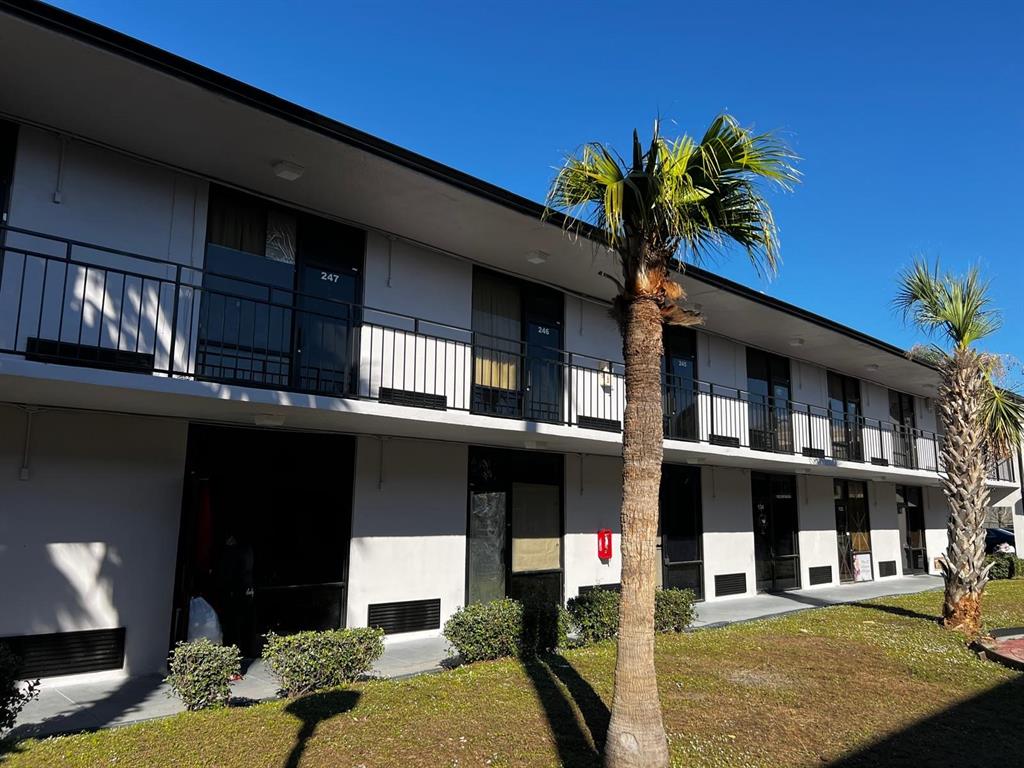 A two-story motel building features exterior walkways with black railings and palm trees in front — 8421 S ORANGE BLOSSOM TRAIL UNIT 441, ORLANDO, FL