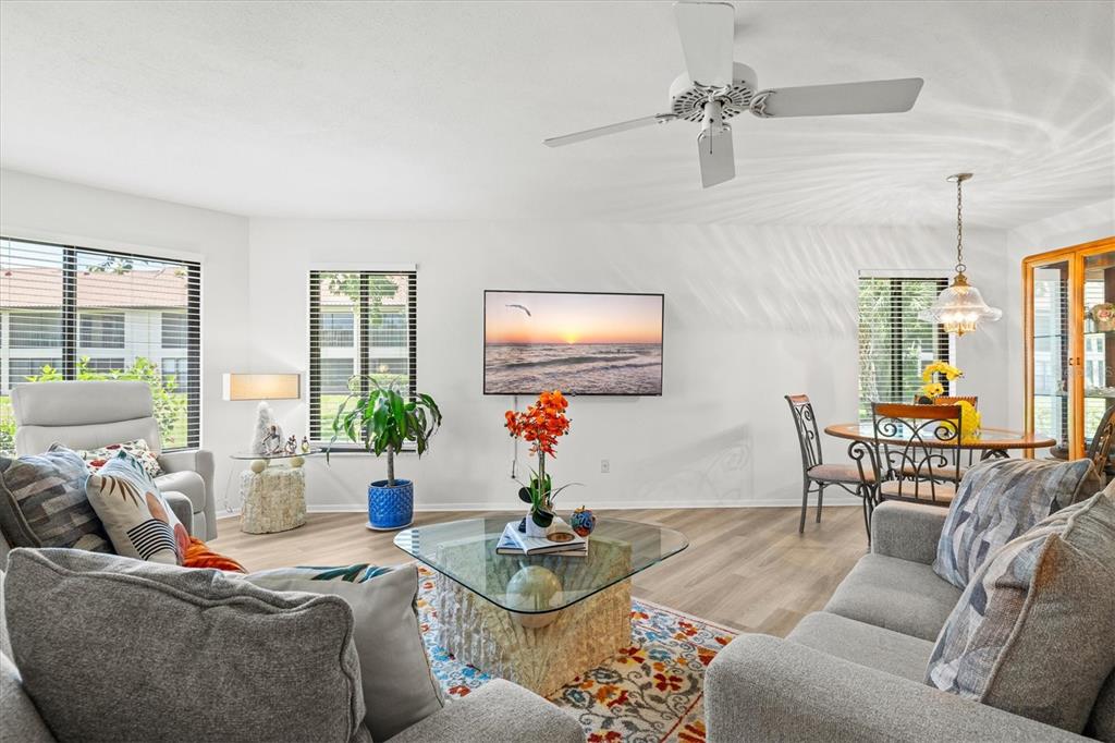 A living room with a glass coffee table, grey sofas, and a wall-mounted television — 792 CAPRI ISLE BLVD UNIT 134, VENICE, FL