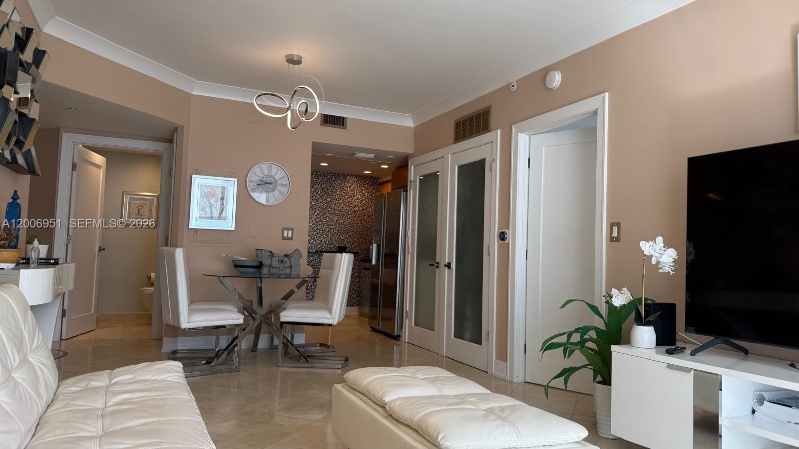 A living and dining area features beige walls, white furniture, and a glass-topped table — 6365 Collins Ave # 906, Miami Beach FL 33141, MIAMI BEACH, FL