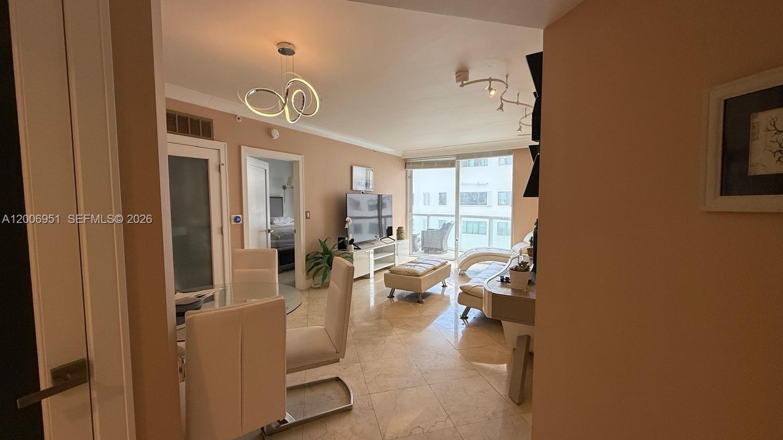 A dining area and living room feature tile floors, modern lighting, and a balcony view — 6365 Collins Ave # 906, Miami Beach FL 33141, MIAMI BEACH, FL