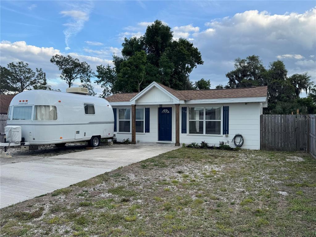 A white single-story house with a blue front door and a parked travel trailer — 135 CARROLL STREET, CLERMONT, FL