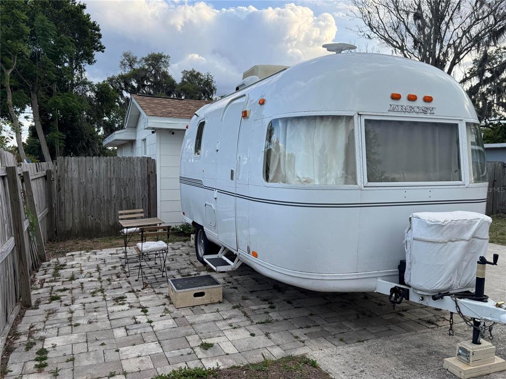 A white Argosy travel trailer is parked on a paved patio next to a wooden fence — 135 CARROLL STREET, CLERMONT, FL