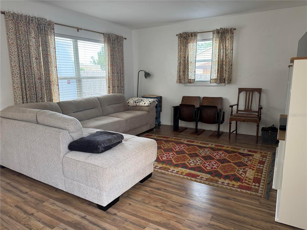 A living room features a gray sectional sofa, a patterned area rug, and wood-look flooring — 135 CARROLL STREET, CLERMONT, FL