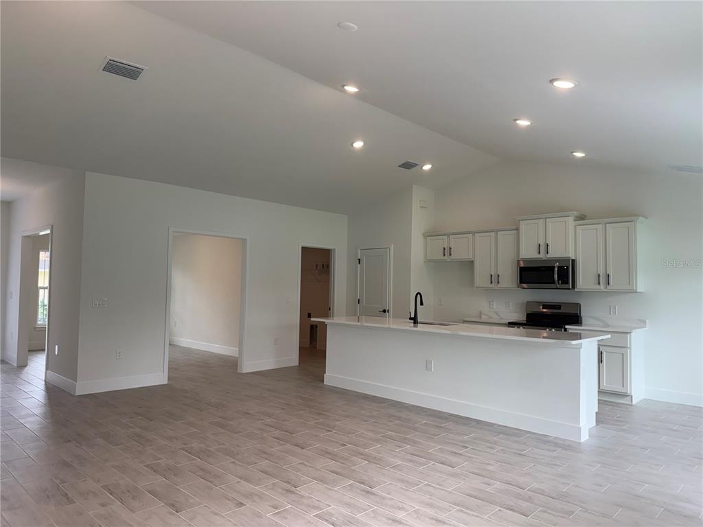 A kitchen with white cabinets and a breakfast bar opens to a living area — 7686 BATTALLA ROAD, NORTH PORT, FL