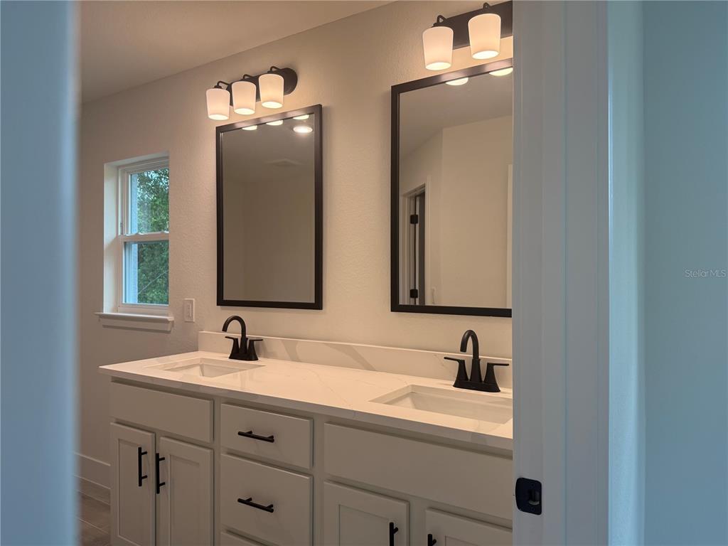 A bathroom features a double vanity with white cabinets, quartz countertops, and black fixtures — 7686 BATTALLA ROAD, NORTH PORT, FL