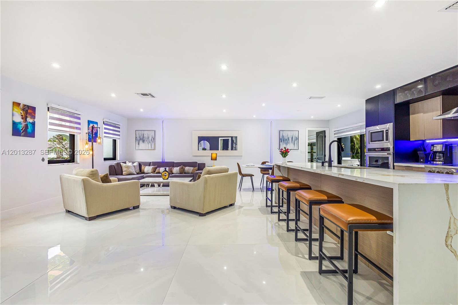 A modern open-concept living room and kitchen featuring white tile floors and leather bar stools — 15331 Turnbull Dr, Miami Lakes FL 33014, MIAMI LAKES, FL
