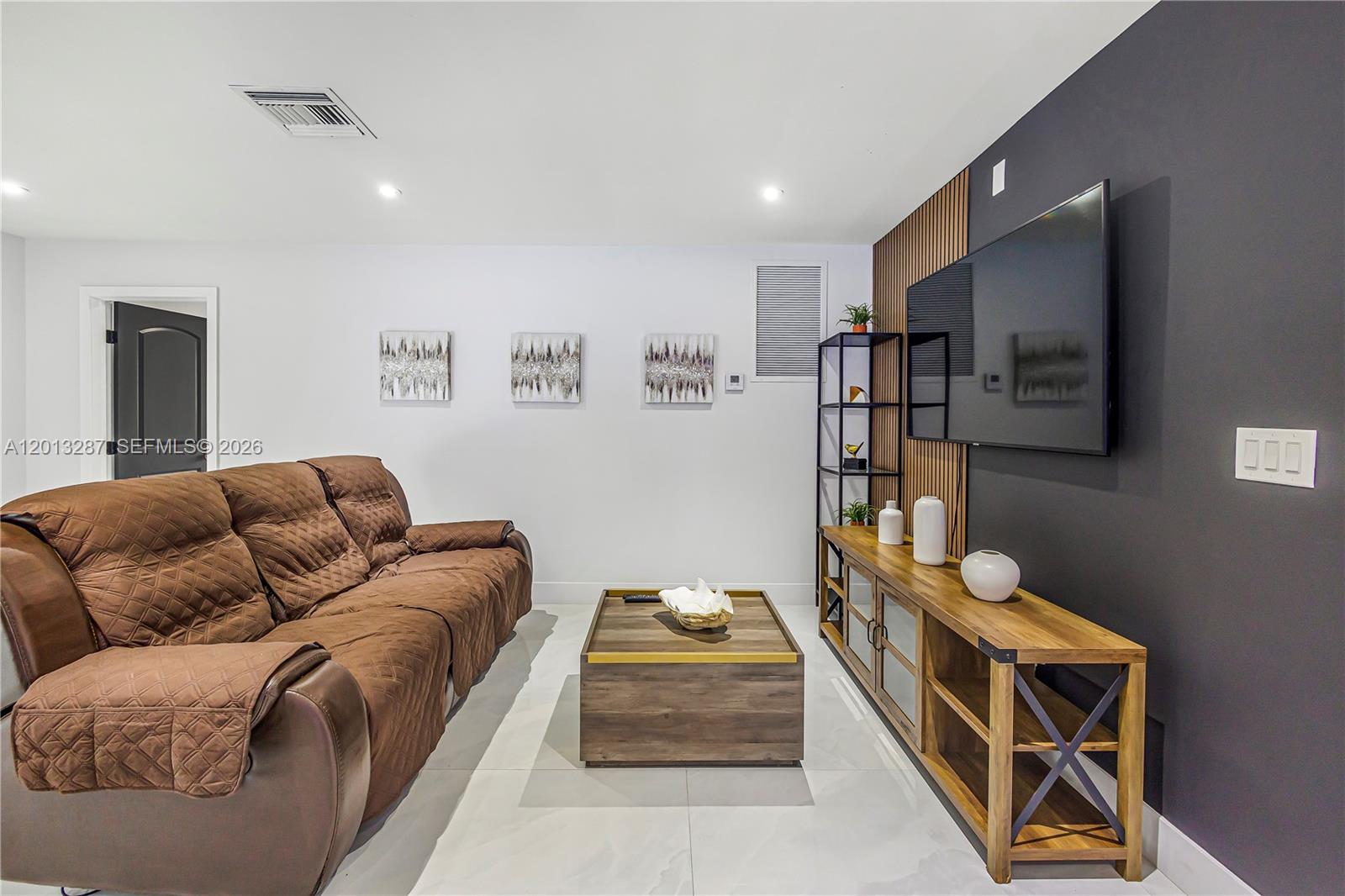 A living room features a brown sofa, a wooden coffee table, and a wall-mounted television — 15331 Turnbull Dr, Miami Lakes FL 33014, MIAMI LAKES, FL