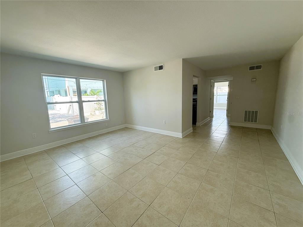 An empty room with light-colored tile flooring, a large window, and a doorway leading outside — 14120 PALM STREET UNIT 104, MADEIRA BEACH, FL