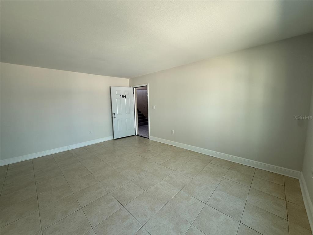 An empty room with light-colored tile flooring and a white door labeled 104 — 14120 PALM STREET UNIT 104, MADEIRA BEACH, FL
