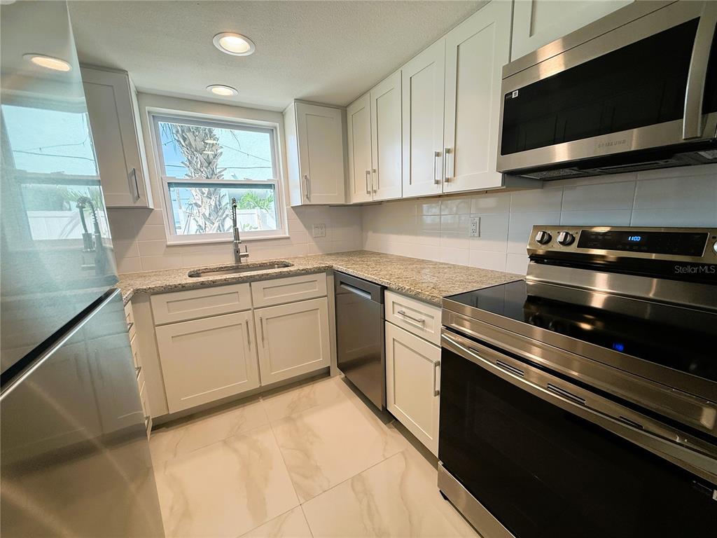A kitchen features white cabinets, granite countertops, stainless steel appliances, and light-colored tile flooring — 14120 PALM STREET UNIT 104, MADEIRA BEACH, FL