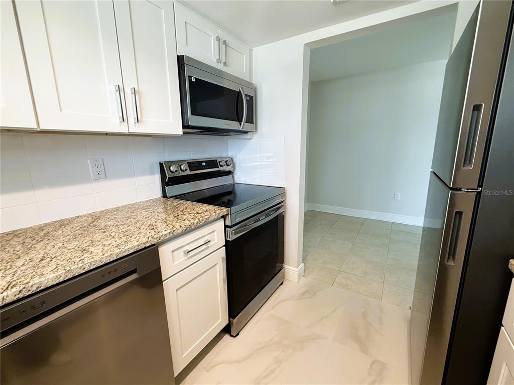 A kitchen features white cabinets, granite countertops, stainless steel appliances, and light tile flooring — 14120 PALM STREET UNIT 104, MADEIRA BEACH, FL