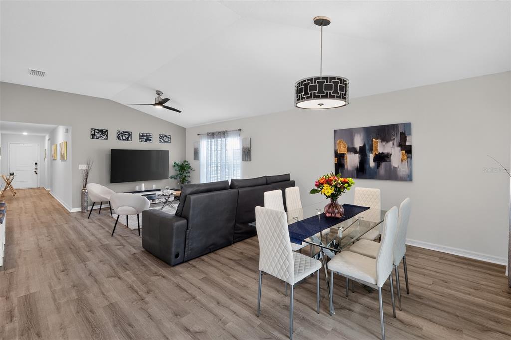 An open-concept living and dining area features wood-look flooring, a vaulted ceiling, and modern furniture — 9181 OSCRAFT DRIVE, DAVENPORT, FL