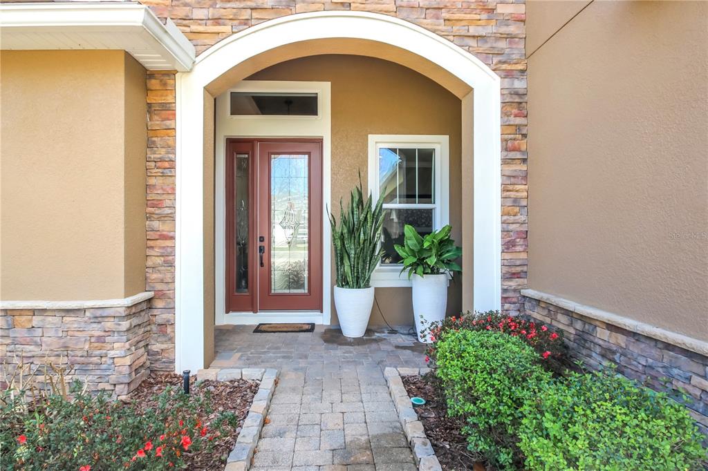 A stone-accented entryway features an arched doorway, a red front door, and two potted plants — 138 OLD MOSS CIRCLE, DELAND, FL