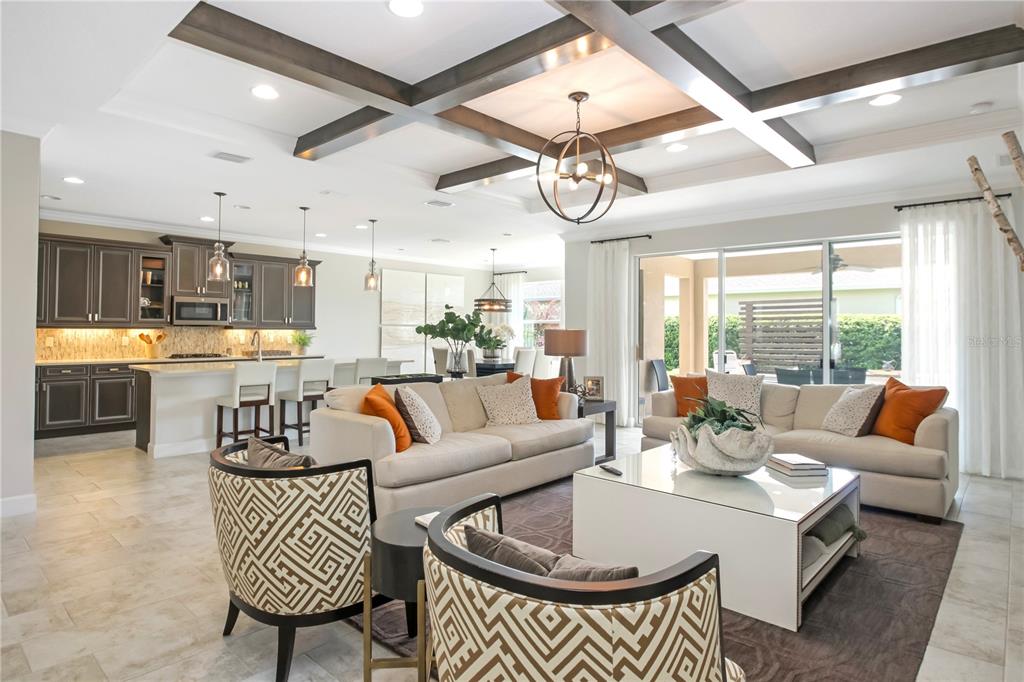 An open-concept living room and kitchen featuring coffered ceilings, tile floors, and neutral furniture — 138 OLD MOSS CIRCLE, DELAND, FL