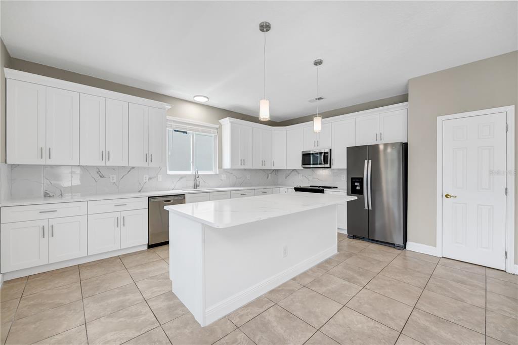 A modern kitchen features white cabinets, a marble-look island, stainless steel appliances, and tile flooring — 200 ANDOVER DRIVE, DAVENPORT, FL