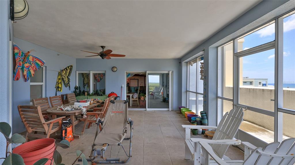 A covered patio features tile flooring, outdoor furniture, colorful butterfly wall art, and screened windows — 5300 S ATLANTIC AVENUE UNIT 5601, NEW SMYRNA BEACH, FL